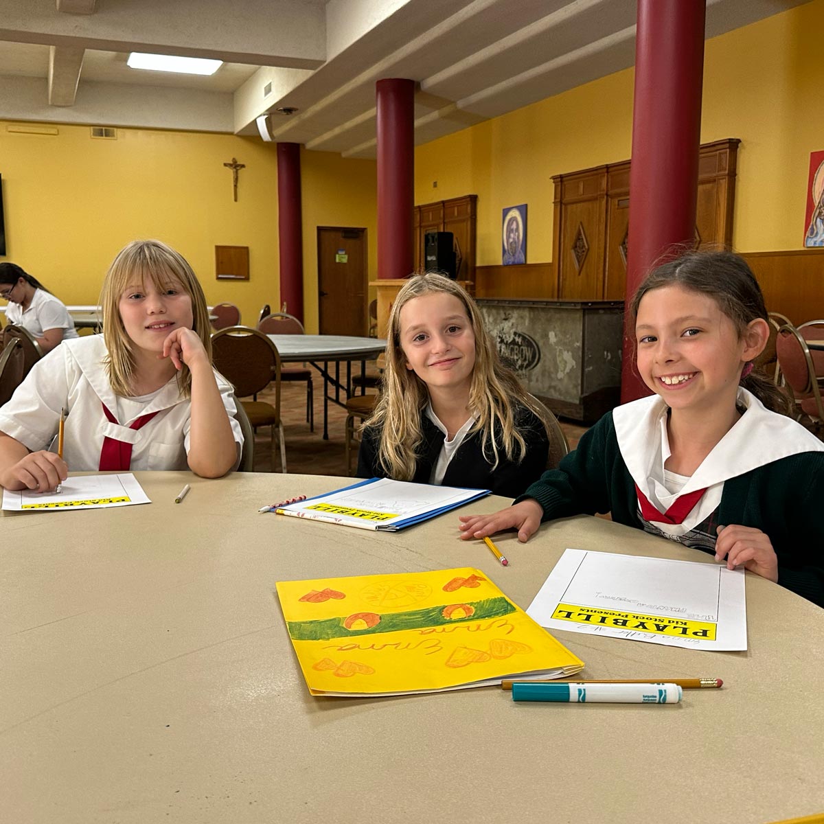 three girls working on playbills at art table
